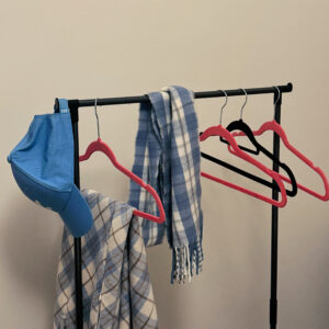 Hangers on a clothing rack with added items, including a blue cap and plaid scarves.