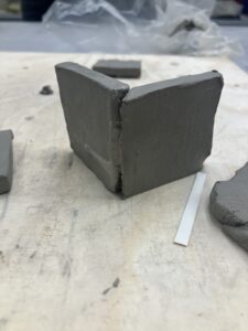 Two small clay slabs standing on their side, perpendicular to one another, are joined roughly on their sides.