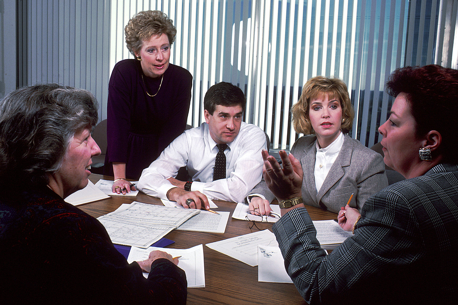 A group of office staff sitting around a table in a meeting, discussing documents — used to illustrate dimension 3 scenario.