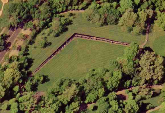 An aerial photograph of the V-shaped Vietnam Veterans Memorial, a long black granite wall embedded in the green landscape of the National Mall.