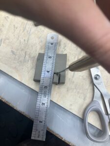 a ruler is guiding a learner cutting a simple doorway shape out of a clay square 