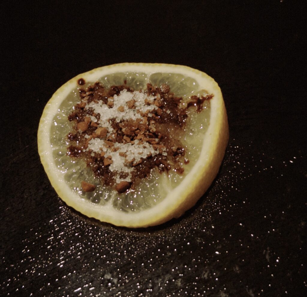A slice of lemon has coffee powder and white granulated sugar on it
