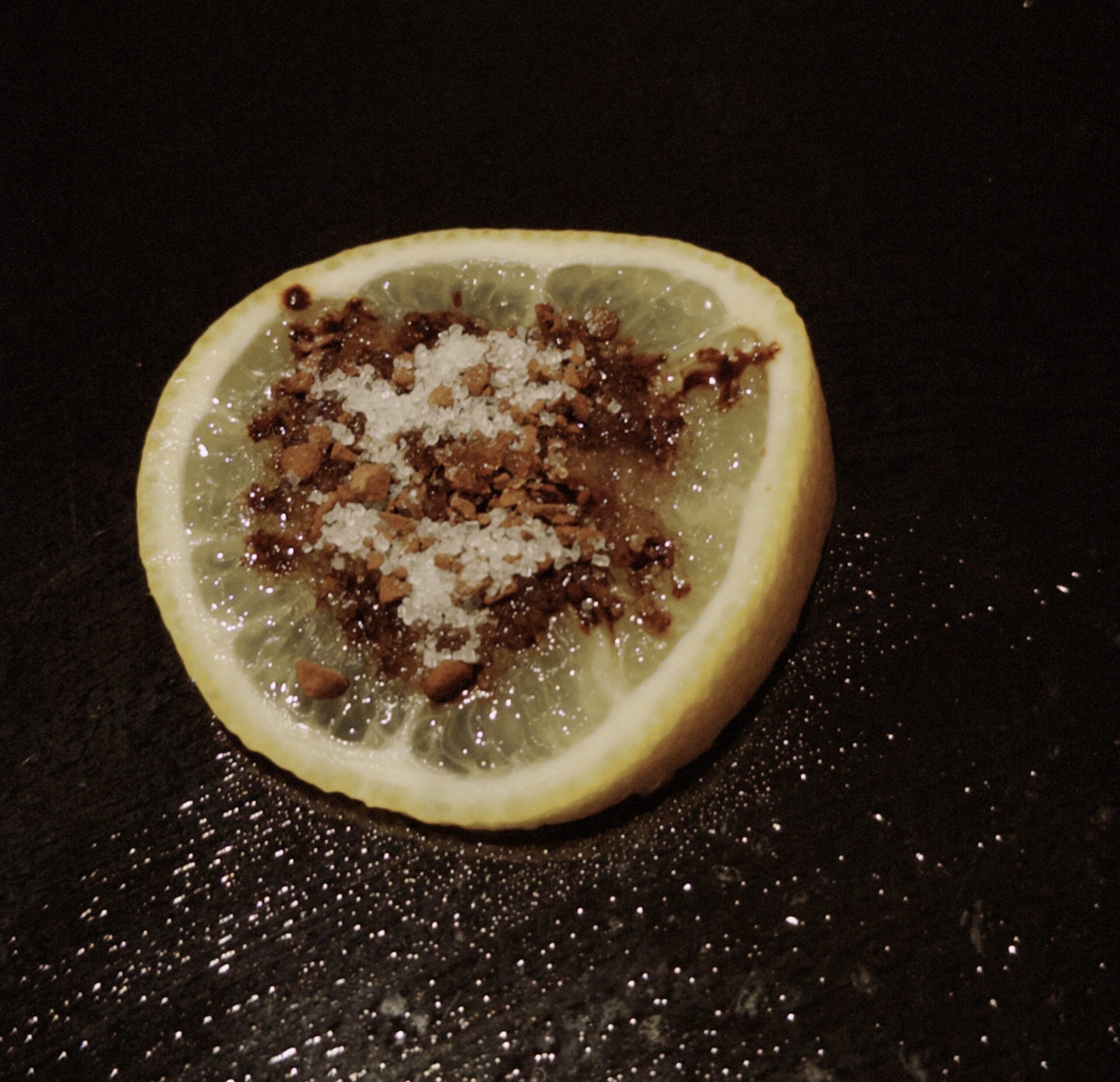 A slice of lemon is sprinkled with coffee powder and white granulated sugar.