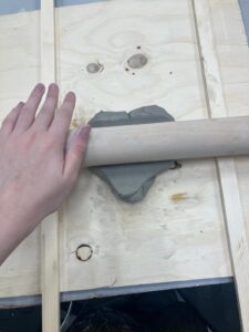 a lump of clay being rolled with a wooden rolling pin with wooden slats either side of it