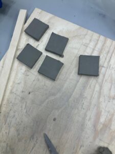 five clay squares of near identical size and shape sit on a wooden board.