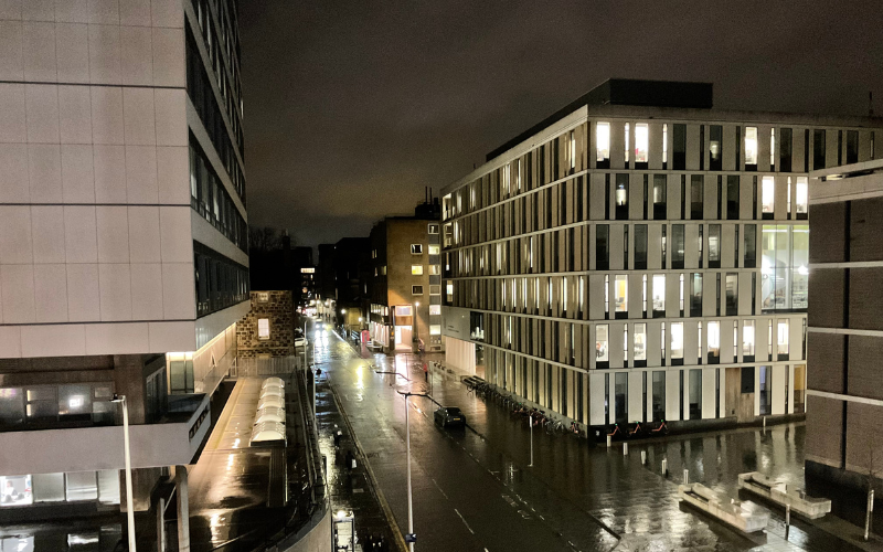 A wide shot of several central campus buildings including Appleton Tower at night. The road below is filled with people, lights and cars.