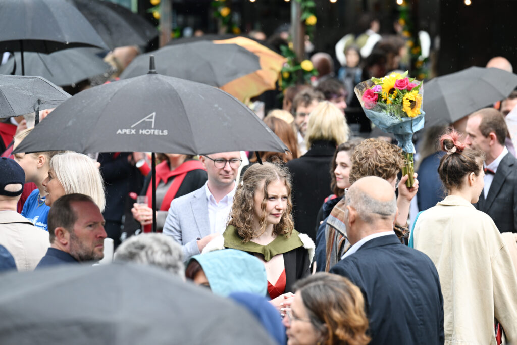 Graduates and their friends and families sheltering under umbrellas at a graduation reception.