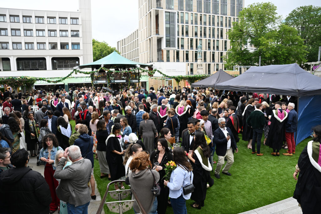 A crowd of graduates and their friends and families celebrating at a graduation reception outside.