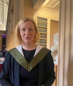 A woman in a graduation gown with a green and white academic hood.