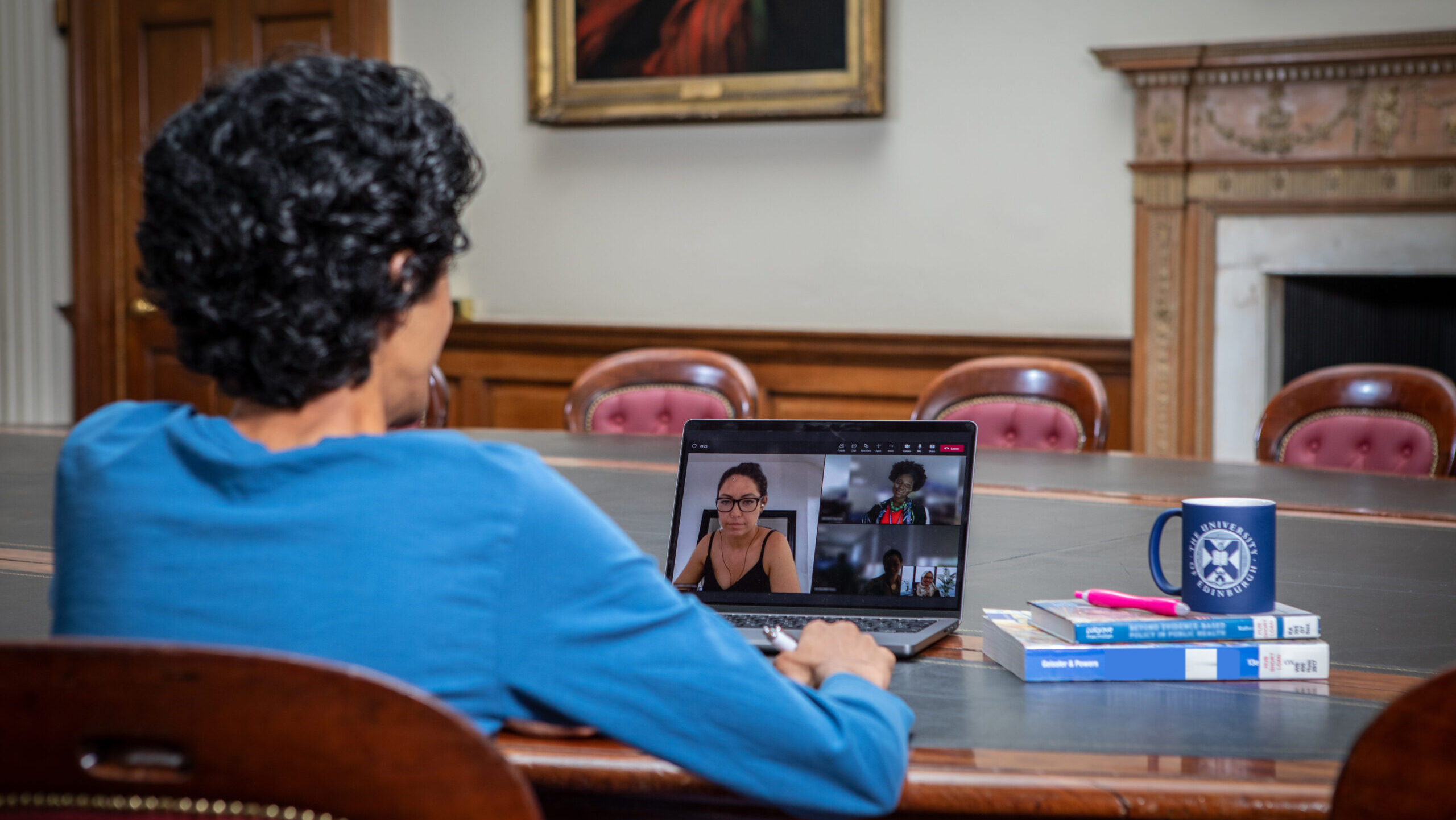 A student shown from behind attending an online lecture on a laptop.