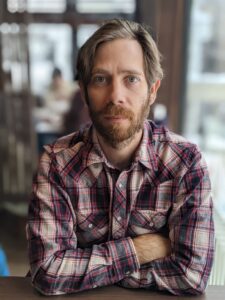 man in plaid shirt looking serious in a coffee shop