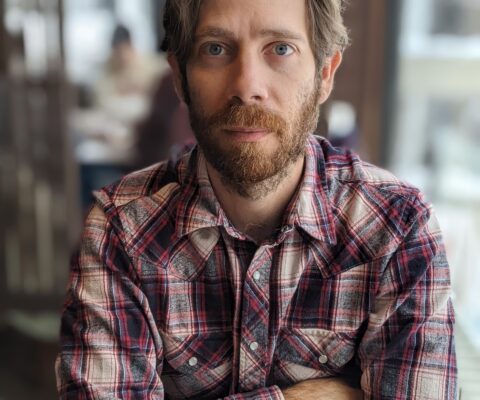man in plaid shirt looking serious in a coffee shop
