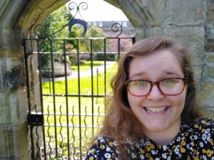 Photo of a smiling white woman wearing glasses in front of an old gate