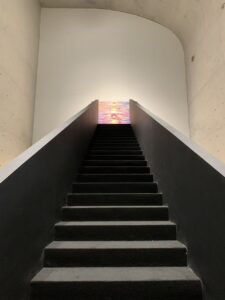 At the end of the long, black staircase stands a contemporary artwork by Huang Yuxing, its colors vibrant and varied.