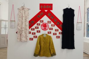 Traditional Chinese garments (Qipao/Tangzhuang) displayed on a white wall.