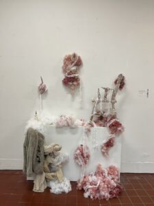 A messy textile installation with pink and white materials on a white wall.