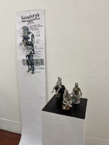 Paper pulp figures on coffee cups next to a large Sainsbury's receipt.