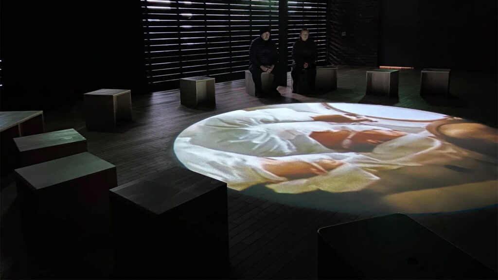 The film is projected onto the floor, featuring archival footage and drone shots that weave together historical fragments and nature-related scenes. Audience seats are arranged in a circular formation around the projection area. You can sit anywhere in the circle, facing the floor to focus on the visuals—like gazing through a "portal" in the ground into the world of the film, and immersively feeling the interplay of history and memory.