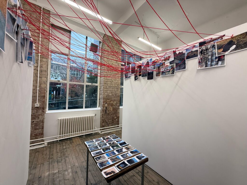 Installation view of Our Shell, showing suspended photographic display with red thread intervention, Summerhall, Edinburgh, 2026. Photograph by Hazel Ren.