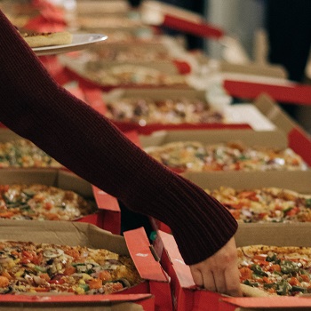 arm reaching out to take slice of pizza from takeaway boxes