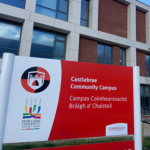 Red and white signpost outside Castlebrae community campus displaying the school's name with building in the background