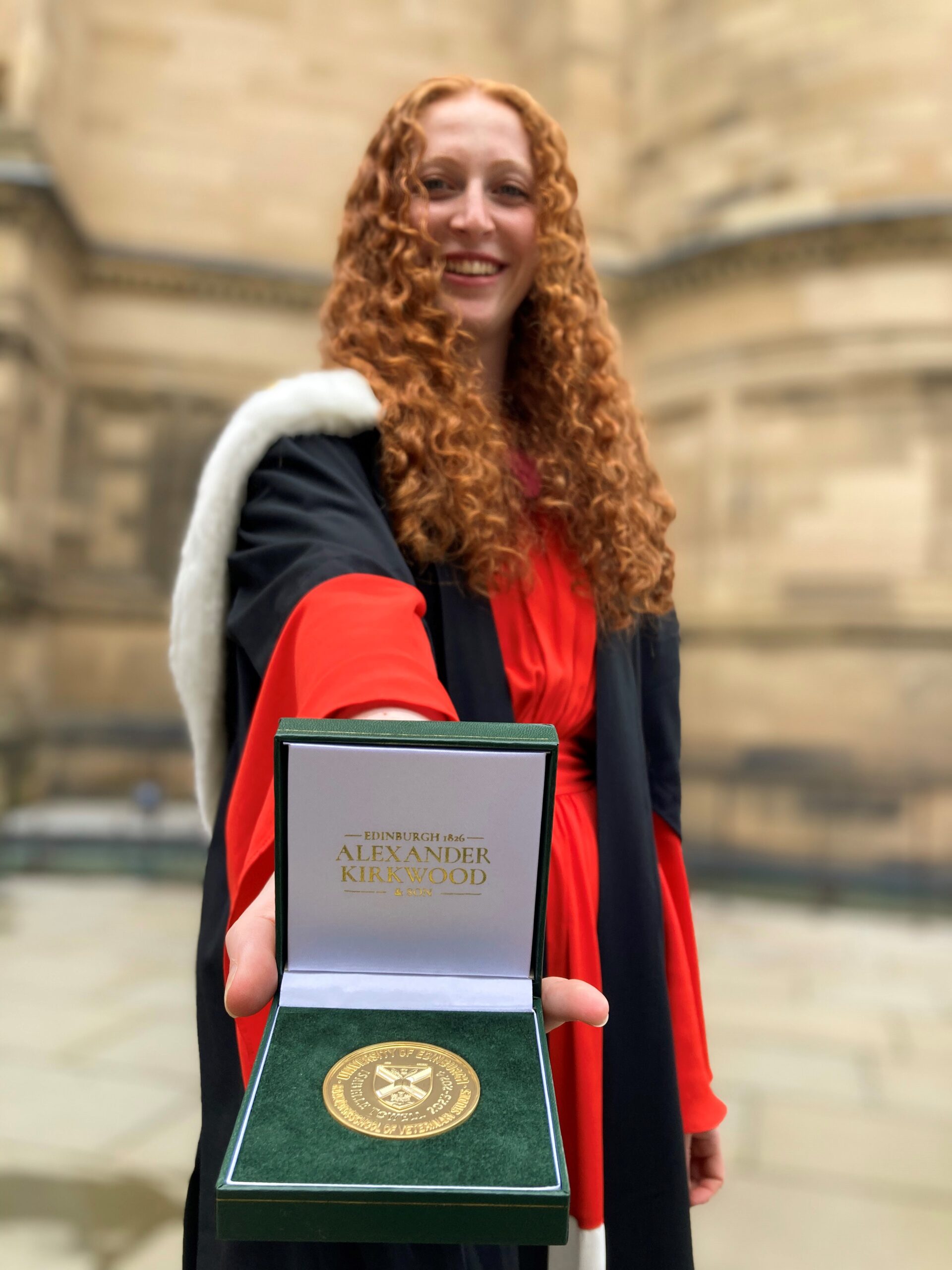 A graduate in her robes displays a medal for the camera.