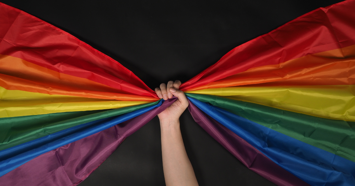A Rainbow flag is grasped in the middle by a hand