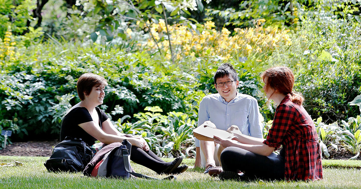 Three students sit in the greenery of George Square