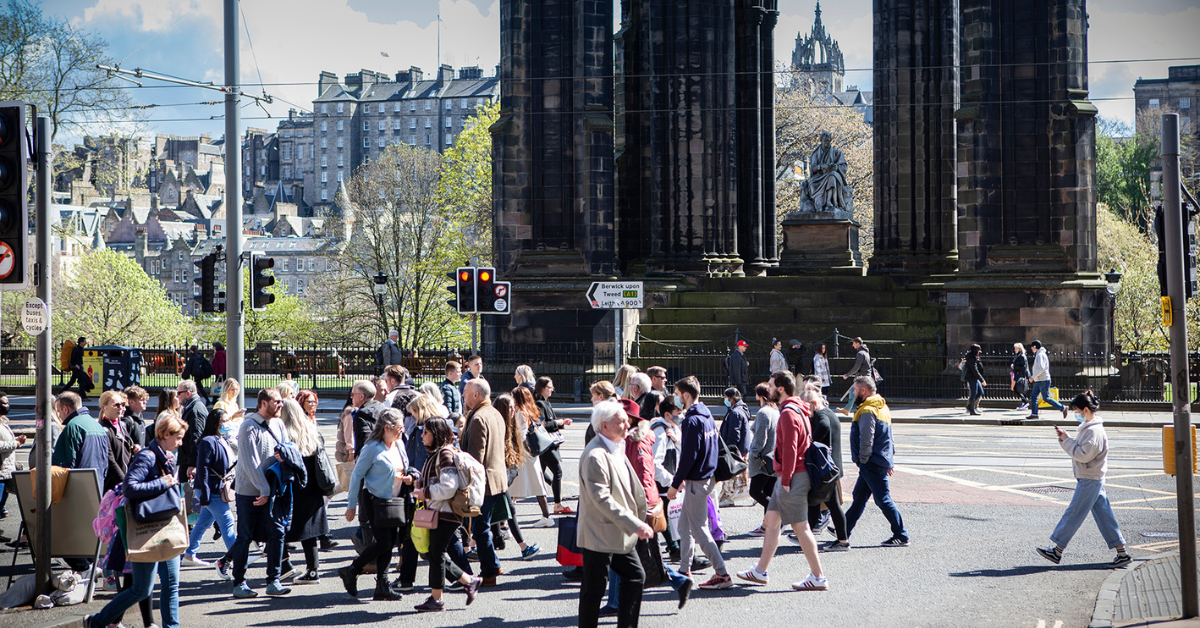 People stream across the road in front of the Scott Monument
