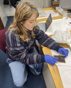 A student, wearing latex gloves, examines three Egyptian statuettes fastened to a card.
