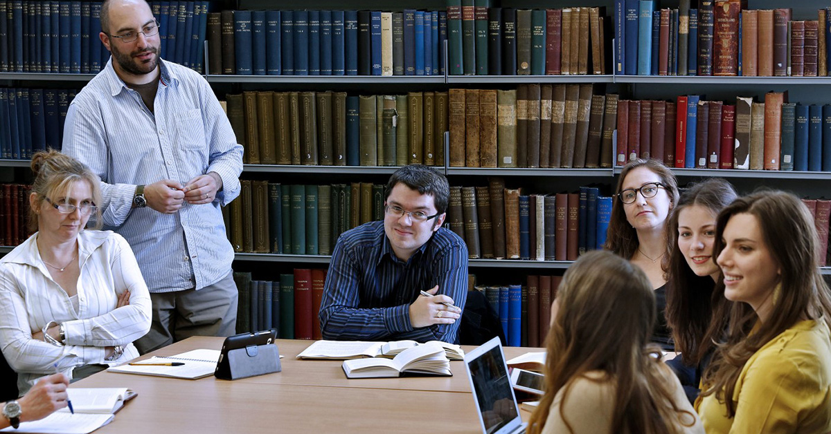 An academic member of staff and students sit around a table in a book-lined room