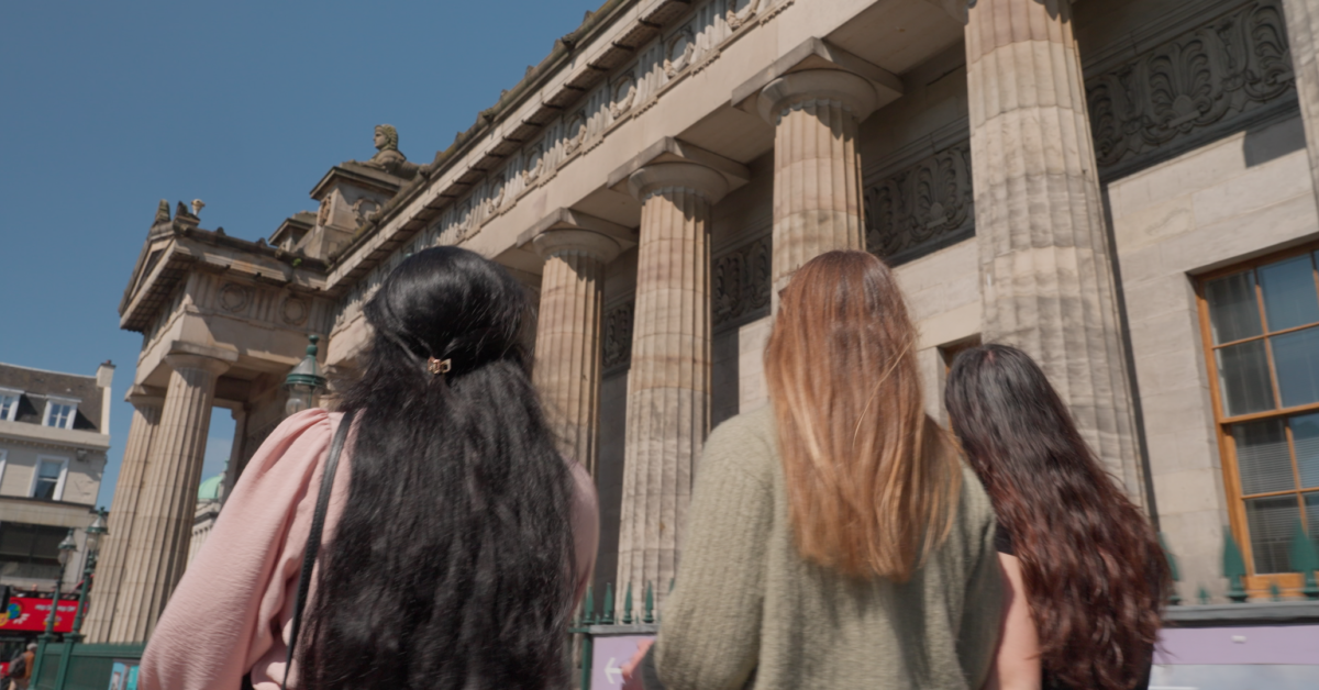 Three young women with long hair walk past the Royal Scottish Academy and its columns
