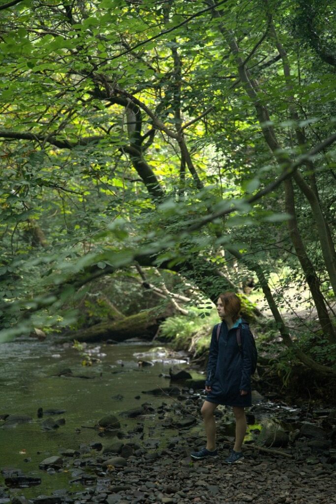 Student standing in a forest near a lake.