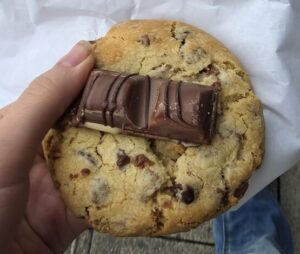 A hand holding a cookie with a chocolate bar in the centre of it.