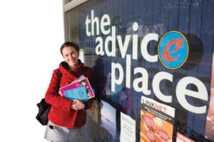 A woman poses in front of a sign that says "The Advice Place," appearing friendly and approachable.