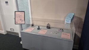 A display case contains small objects and informational sheets, with a sign and pamphlets on the side.