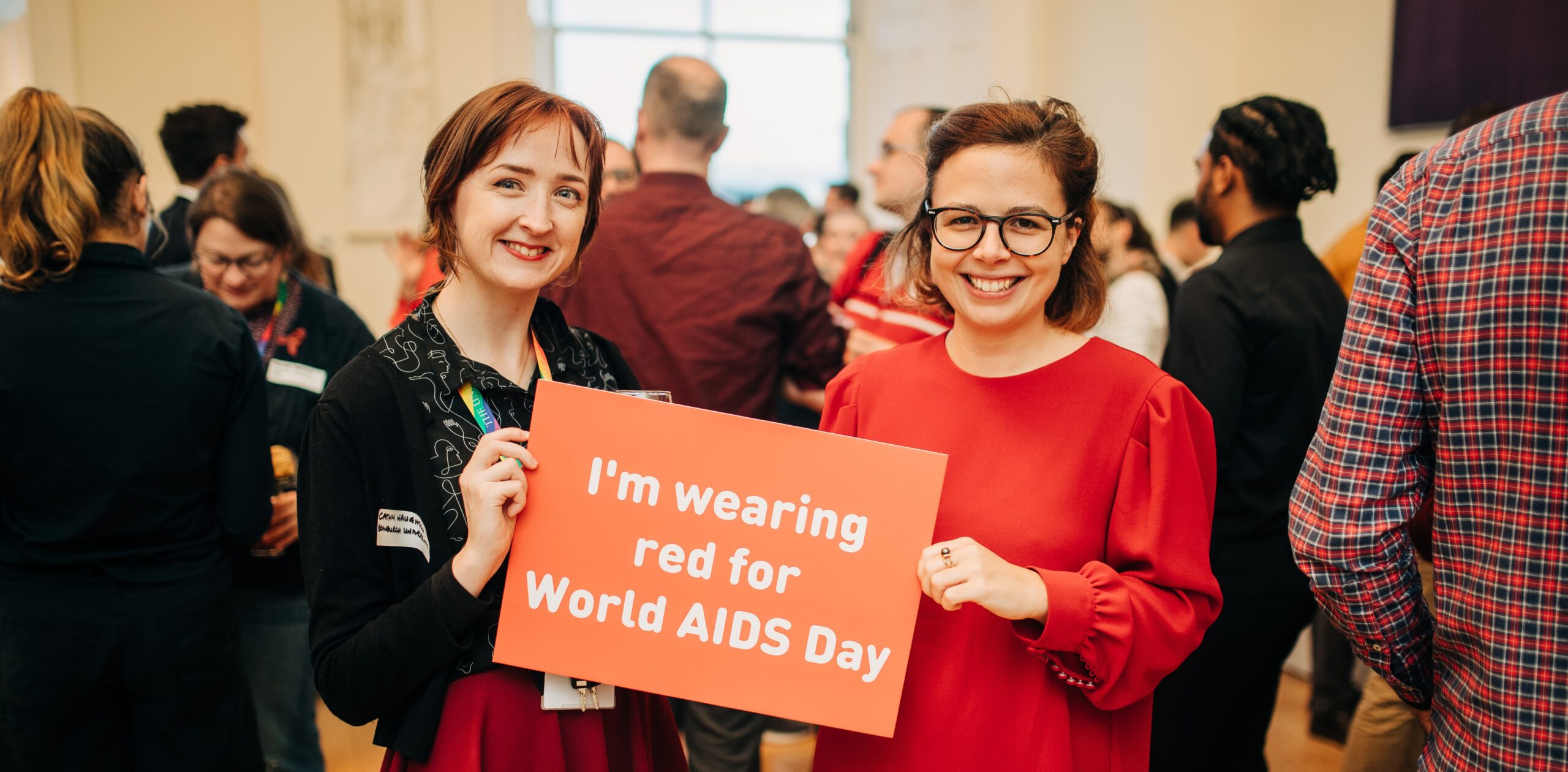 Staff Pride Network committee members at an event hosted by Waverley Care, holding a sign that reads "I'm wearing red for World Aids Day"
