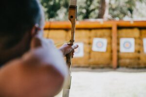 A person aiming a bow and arrow at a wall of targets