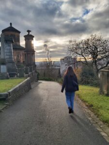 Image shows someone strolling through the Glasgow Necropolis, with the city's skyline in the distance. 