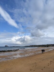 Image shows two people strolling down the sunny beach at North Berwick. 