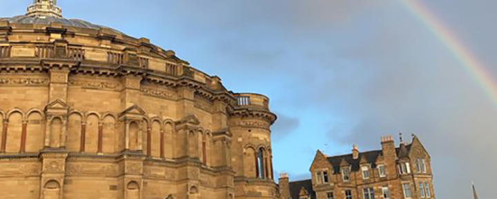 Roofline of McEwan Hall with a rainbow in the sky above.