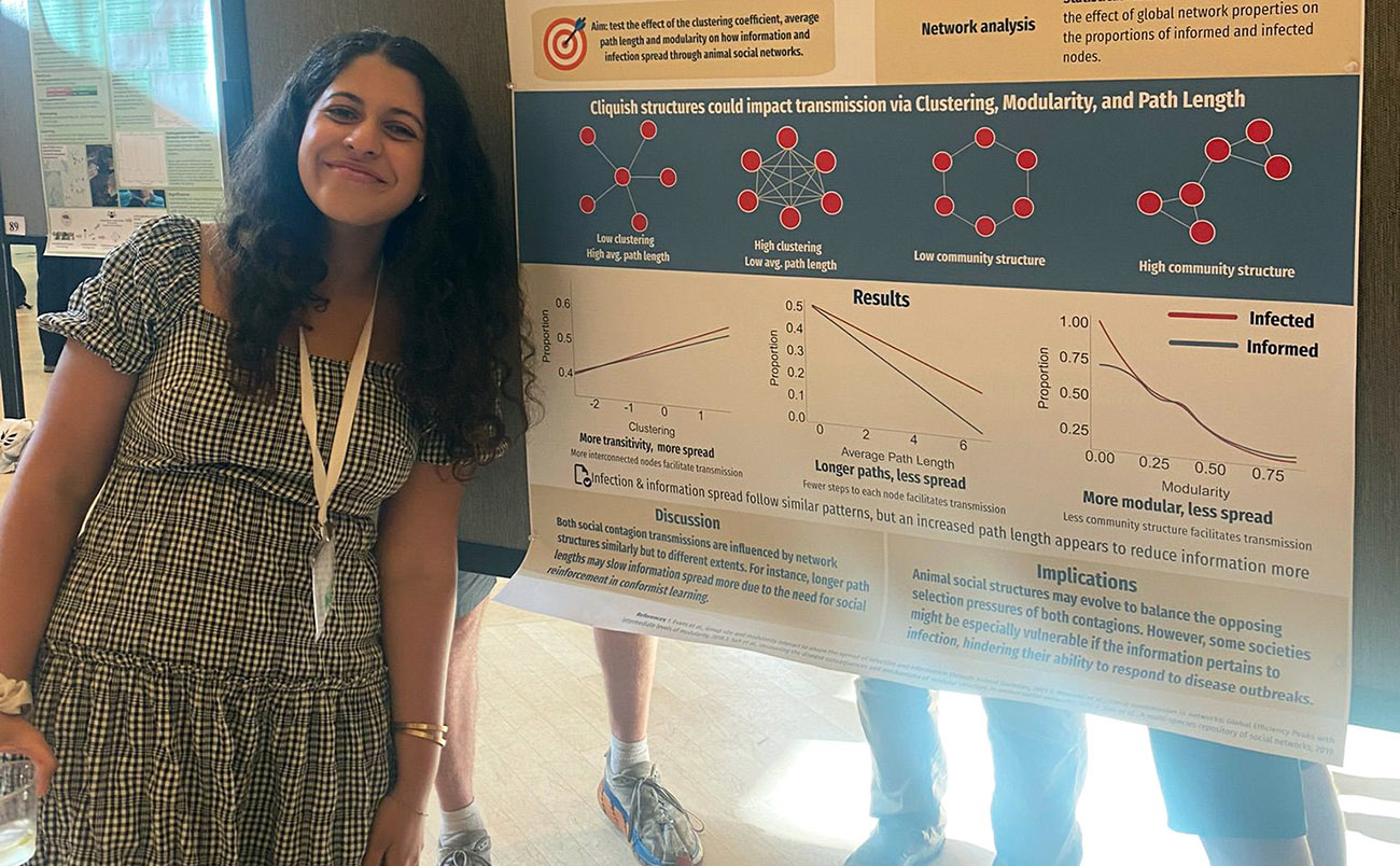 A student stands, smiling in front of a poster.