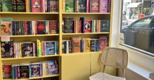 A bookshop with a chair in front of a bright yellow bookcase filled with books.