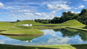An image of green hills by a body of water, with blue skies in the background.