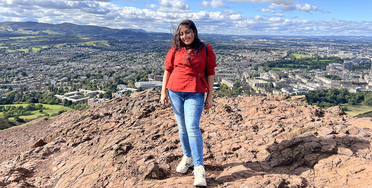 A smiling student stands at the top of a hill. The sun is shining.