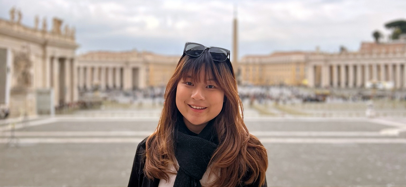 A student stands in a grand square smiling.