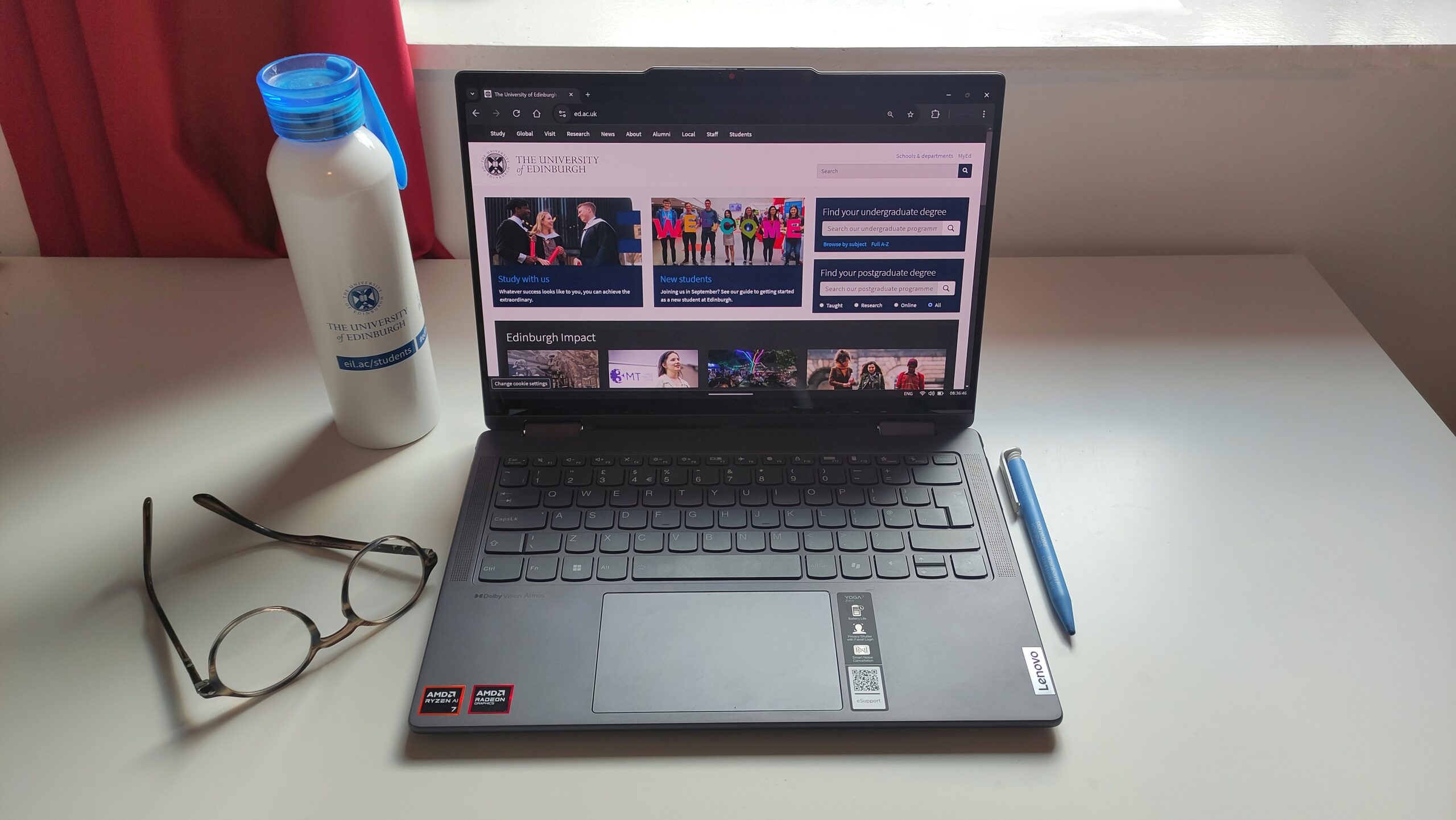 A student's work space with a laptop, glasses, pen and water bottle.