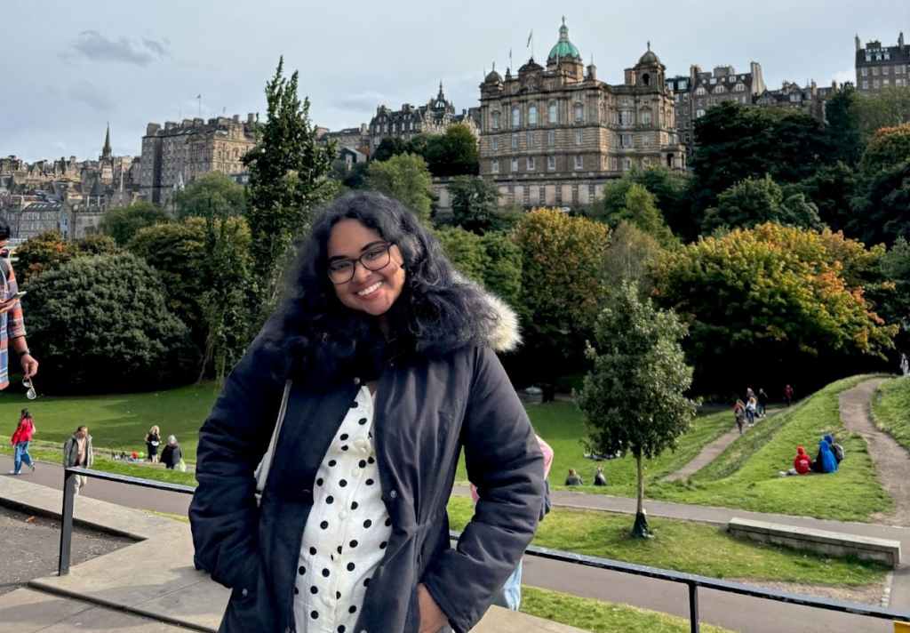 Sanchita standing in front of Princes Street Gardens with Edinburgh Castle in the background.