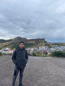 Omkar smiling to camera in front of Edinburgh Skyline.