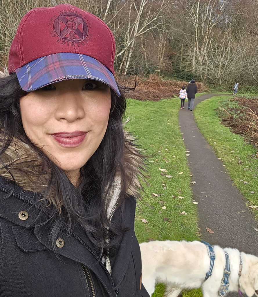 Jolina wearing University of Edinburgh-branded cap while walking dog in the park.